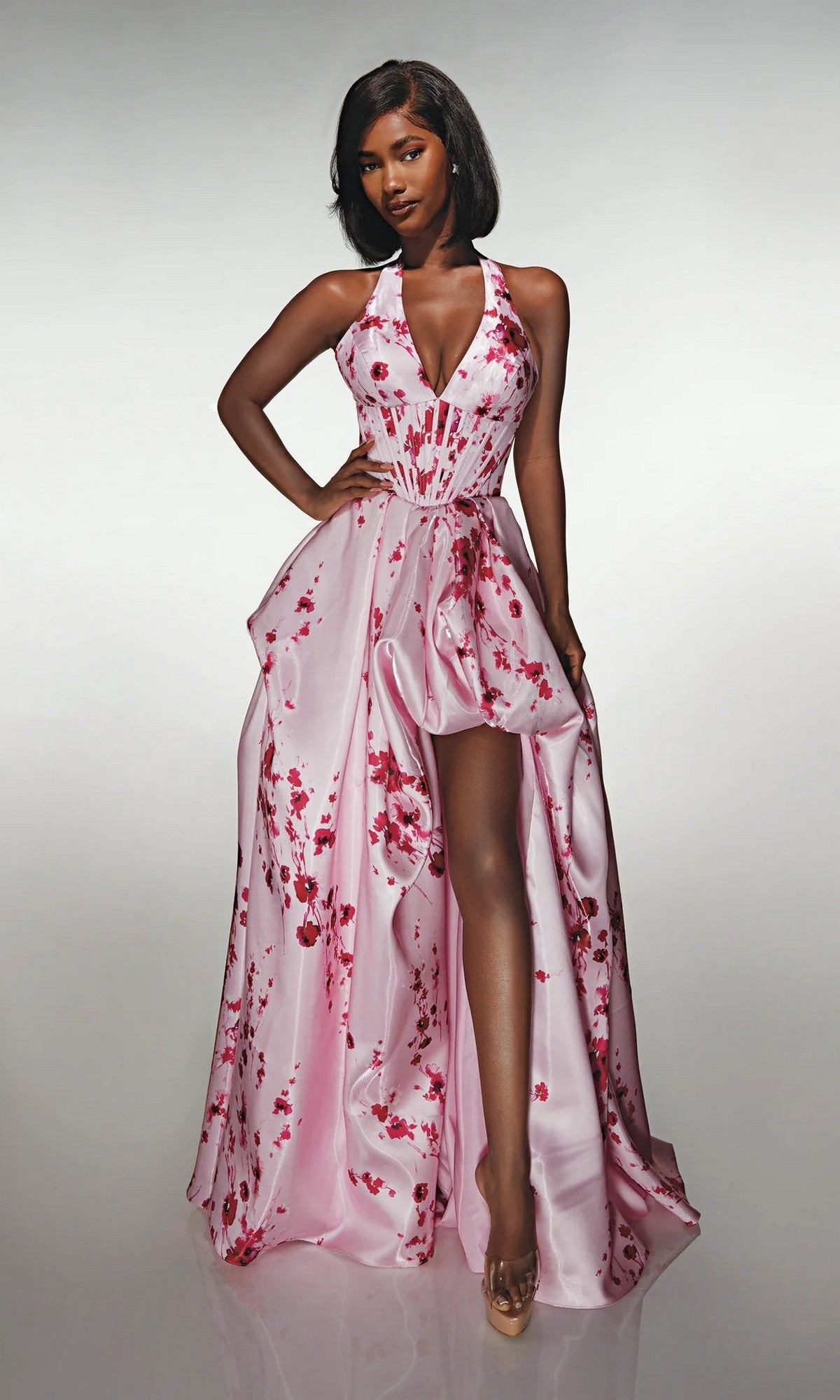 A woman poses confidently in the Alyce 62214 long formal dress, featuring a sleeveless pink corset bodice, red floral accents, and a high slit, set against a plain light background.